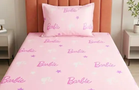 Barbie Star Single Bedsheet on bed with pillow, pink 100% cotton sheet set featuring purple Barbie logos and white stars on peach headboard